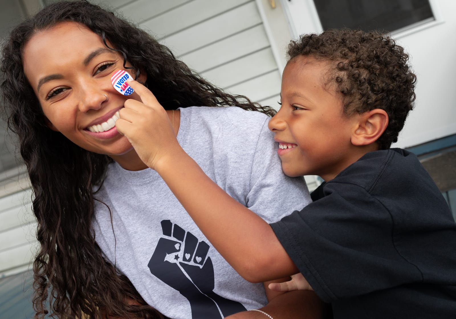 Black mother wearing BLM t-shirt with child holding up an I voted sticker