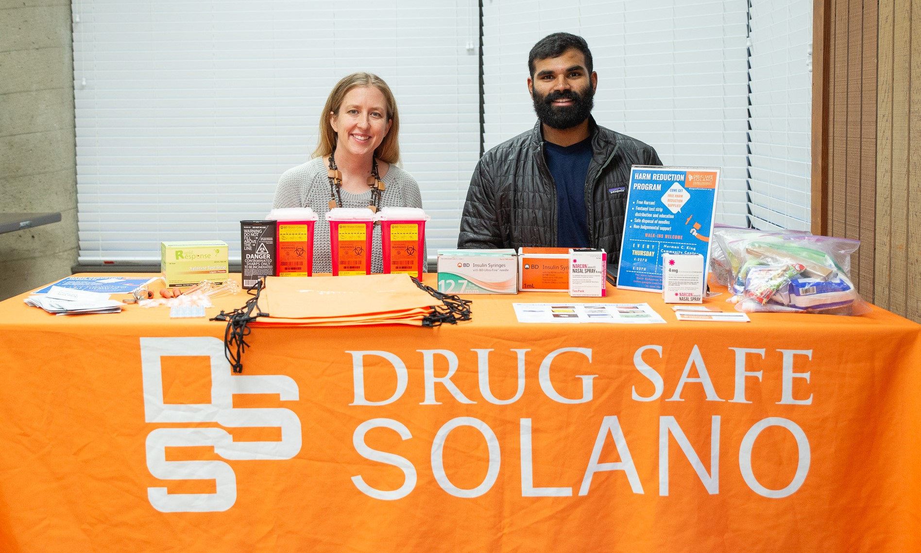 Dr. Christina Kinnevey-Greig sitting at the Harm Reduction table inside the Student Run Free Clinic next to student doctor Amrit Banga