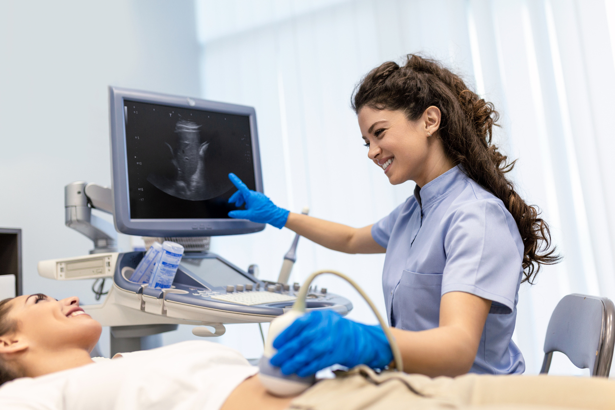 Sonography technician uses the imaging machine on a pregnant woman\'s belly to see the image of the fetus inside